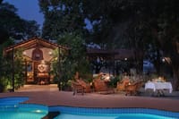 Cane chairs around a firepit beside the pool at dusk at Jaagir Manor, Dudhwa