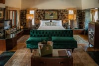 The Plunge Pool Villa bedroom with green velvet sofa, stone walls and blackbuck painting at The Blackbuck Lodge, Velavadar