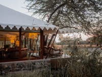White canvas-roofed lounge with leather sofas and lanterns hanging from an acacia tree at dusk at The Blackbuck Lodge, Velavadar