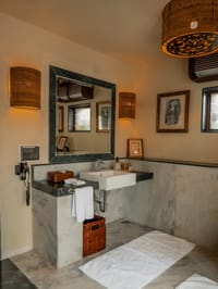 The Villa bathroom with marble vanity, green stone-framed mirror and wicker light shades at The Blackbuck Lodge, Velavadar