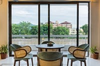 Cafe table with cane and velvet chairs by floor-to-ceiling windows overlooking the Ganga at Ekaanta, Haridwar