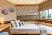 Pod bedroom with double bed, patterned wall panel and corner window at Ekaanta, Haridwar