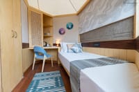 Pod interior with single bed, desk with blue chair and cane-fronted wardrobe at Ekaanta, Haridwar