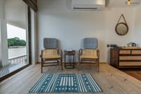 Room sitting area with two cushioned cane chairs and balcony door overlooking the Ganga at Ekaanta, Haridwar