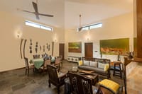 Lounge with carved wooden seating, dining table and butterfly canvases at Singinawa Jungle Lodge, Kanha