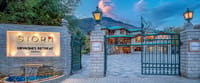 Stone gateposts and wrought-iron gates at the entrance, with the hotel and mountains behind at dusk, at Storii Urvashi's Retreat, Manali