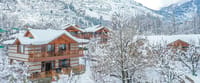 Snow-covered stone-and-wood chalets among bare trees on a white hillside in winter at Storii Urvashi's Retreat, Manali