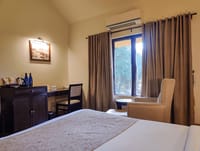 Bedroom with writing desk, armchair by the window and dark wood furniture at WelcomHeritage Tadoba Vanya Villas, Tadoba