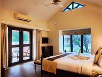 Bedroom with vaulted ceiling, stained-glass gable window, king bed and garden-facing picture windows at WelcomHeritage Tadoba Vanya Villas, Tadoba