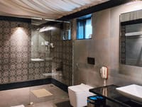 Tented bathroom at WelcomHeritage Tadoba Vanya Villas with patterned tiles, glass walk-in shower and basin on a black stone counter
