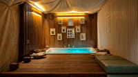 Sunken jacuzzi bath under a canvas canopy with wood-slat walls and cushioned benches at WelcomHeritage Tadoba Vanya Villas