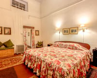 Ada Villa bedroom with high ceilings, rose-print bedspread and curtains, framed prints and Persian rugs at Windamere Hotel, Darjeeling