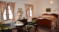 Chogyal of Sikkim room at Windamere Hotel with a wooden double bed, cane-backed armchairs and floral curtains at twin windows