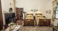 Prince Peter of Greece and Denmark room at Windamere Hotel with twin beds, a dark fireplace and a coffee table with fruit and wine