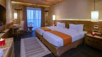 Deluxe Rooms twin beds with orange runners, stone walls and a timber ceiling at Sarangkot Mountain Lodge, Pokhara