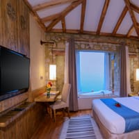 Suites room with exposed beams, a bathtub by the picture window and a bed with a blue runner at Sarangkot Mountain Lodge, Pokhara