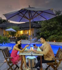 Couple dining under an umbrella beside the lit pool at dusk at Barahi Jungle Lodge, Chitwan