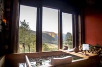 Traditional wooden hot stone bath strewn with petals beside windows with valley views at Gangtey Lodge, Gangtey
