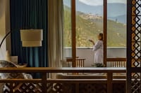 Balcony Room guest in a robe having tea on the private balcony overlooking the valley at Bhutan Spirit Sanctuary, Paro