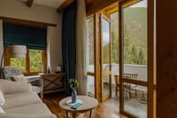 Balcony Room sitting area with a sofa, armchair and folding doors opening to a private balcony with mountain views at Bhutan Spirit Sanctuary, Paro