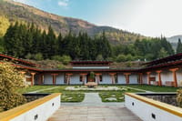 Courtyard with lawns, stone paths and covered walkways framed by hills at Bhutan Spirit Sanctuary, Paro