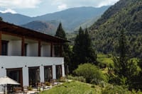 Guest-room wing with covered balconies and terrace seating above a green valley at Bhutan Spirit Sanctuary, Paro