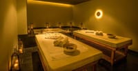 Candle-lit spa treatment room with two massage tables and a bath at Bhutan Spirit Sanctuary, Paro