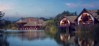 Thatched Water Dwellings on stilts reflected in the lake at dusk at Jetwing Vil Uyana, Sigiriya