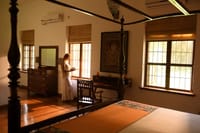 Bedroom with a four-poster bed, carved wooden writing desk and sunlit windows at Svatma, Thanjavur