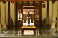 Bronze deity statue ringed with marigold flowers in a stone-pillared hall at Svatma, Thanjavur