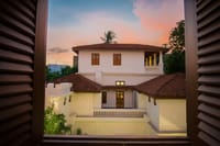 White heritage building with terracotta-tiled roofs seen through wooden shutters at sunset at Svatma, Thanjavur