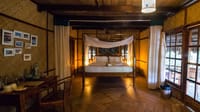 Fan Cooled Duplex Cottage four-poster bed with white canopy, woven walls, framed photographs and writing desk at Barefoot at Havelock, Havelock