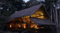 Two-storey thatched lounge bar glowing with lights at dusk among forest trees at Barefoot at Havelock, Havelock