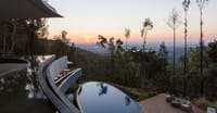 Curved infinity pools and deck looking over forested hills to the sunset at Java Rain Resort, Chikmagalur