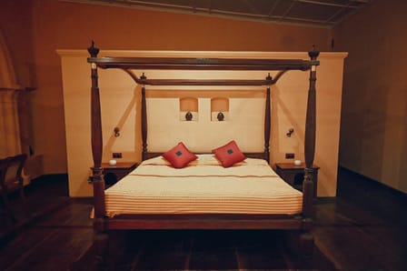 Suite at Old Harbour Hotel: carved four-poster bed with red cushions in a high-ceilinged room