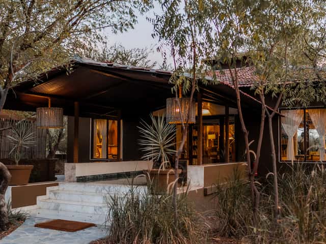 Lodge building with red-tiled roof, marble steps and lantern-lit veranda among dry grasses at dusk at The Blackbuck Lodge, Velavadar