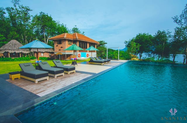 Infinity pool with sun loungers and umbrellas in front of a brick-and-tile building beside the lake at Anantya by the Lake, Chittar
