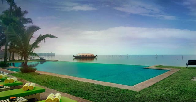 Infinity pool merging into Vembanad Lake with a houseboat beyond and loungers on the deck, Kumarakom Lake Resort, Kumarakom
