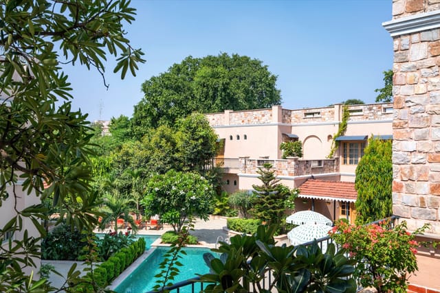 Stone-clad Estate wing and tiled pool seen through frangipani and palms, Niravi, Jaipur