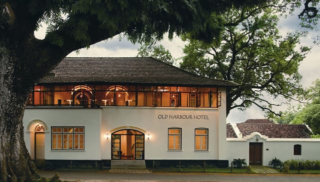 Old Harbour Hotel, Fort Cochin: the white two-storey Dutch-style mansion with tiled roof under a large rain tree, upper windows lit at dusk