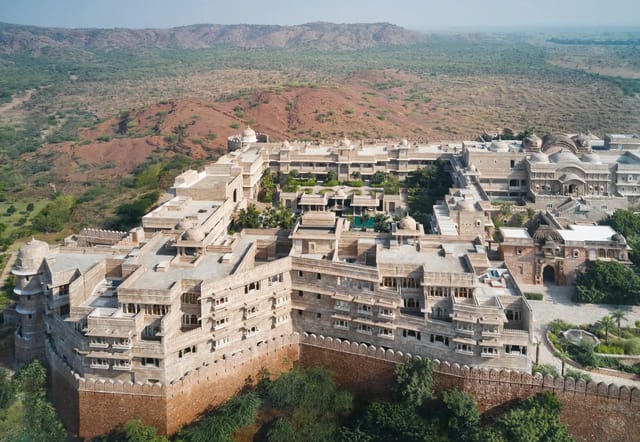 Aerial view of the whole walled fort: ramparts, domes, courtyards and pool, with the Aravali landscape behind. No people.