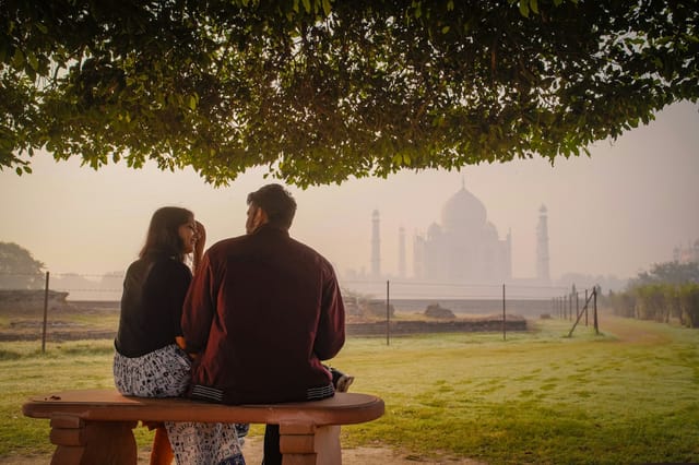 A couple on a bench looking out to the Taj Mahal in the morning haze