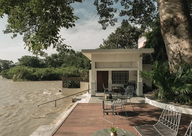 Riverside terrace and private ghat beside the flowing Ganga, shaded by a large tree, at Amrit Bhawan, Haridwar