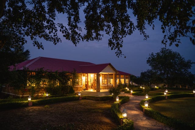 The lodge lit at dusk under the trees, the paths lantern-lit