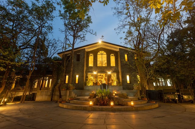 Stone main lodge lit with lanterns at dusk, safari jeeps parked to the side at Singinawa Jungle Lodge, Kanha