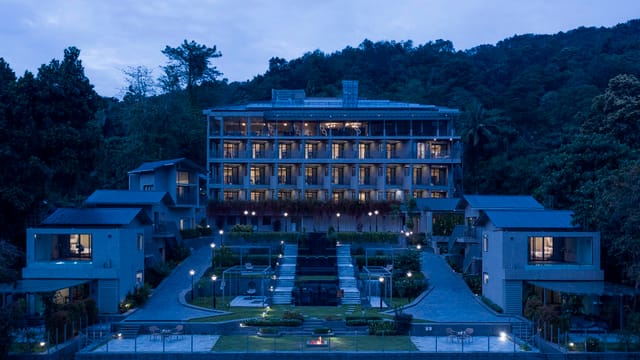 Main retreat building and villas lit up at dusk against a forested hillside at Niraamaya Retreats Samroha, Athirappilly