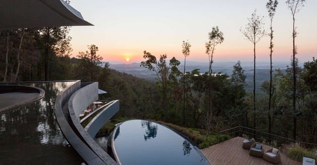 Curved infinity pools and deck looking over forested hills to the sunset at Java Rain Resort, Chikmagalur