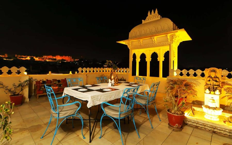 Rooftop restaurant table at night with lit chhatri and fort view