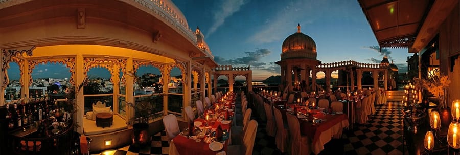 Candle-lit dinner tables on the rooftop terrace at dusk under domes and chhatris