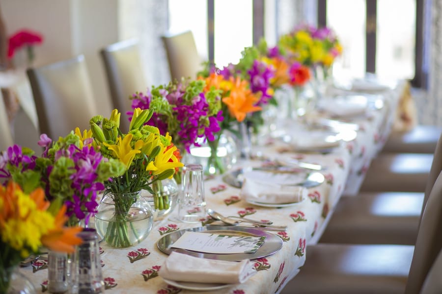 Long banquet table set with colourful lily and orchid arrangements on block-print linen